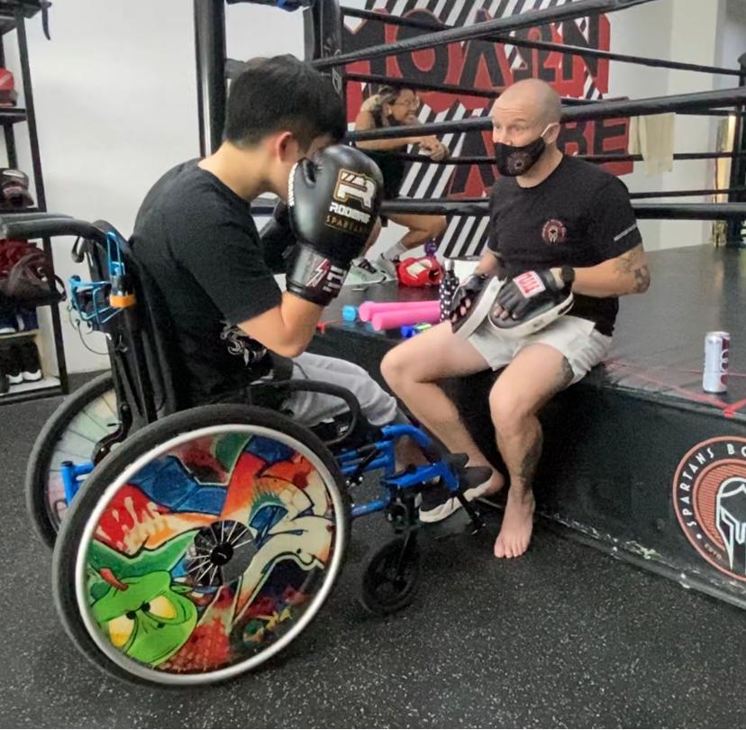 Photo shows Keith in wheelchair having a post-session debrief with his boxing coach after his training.